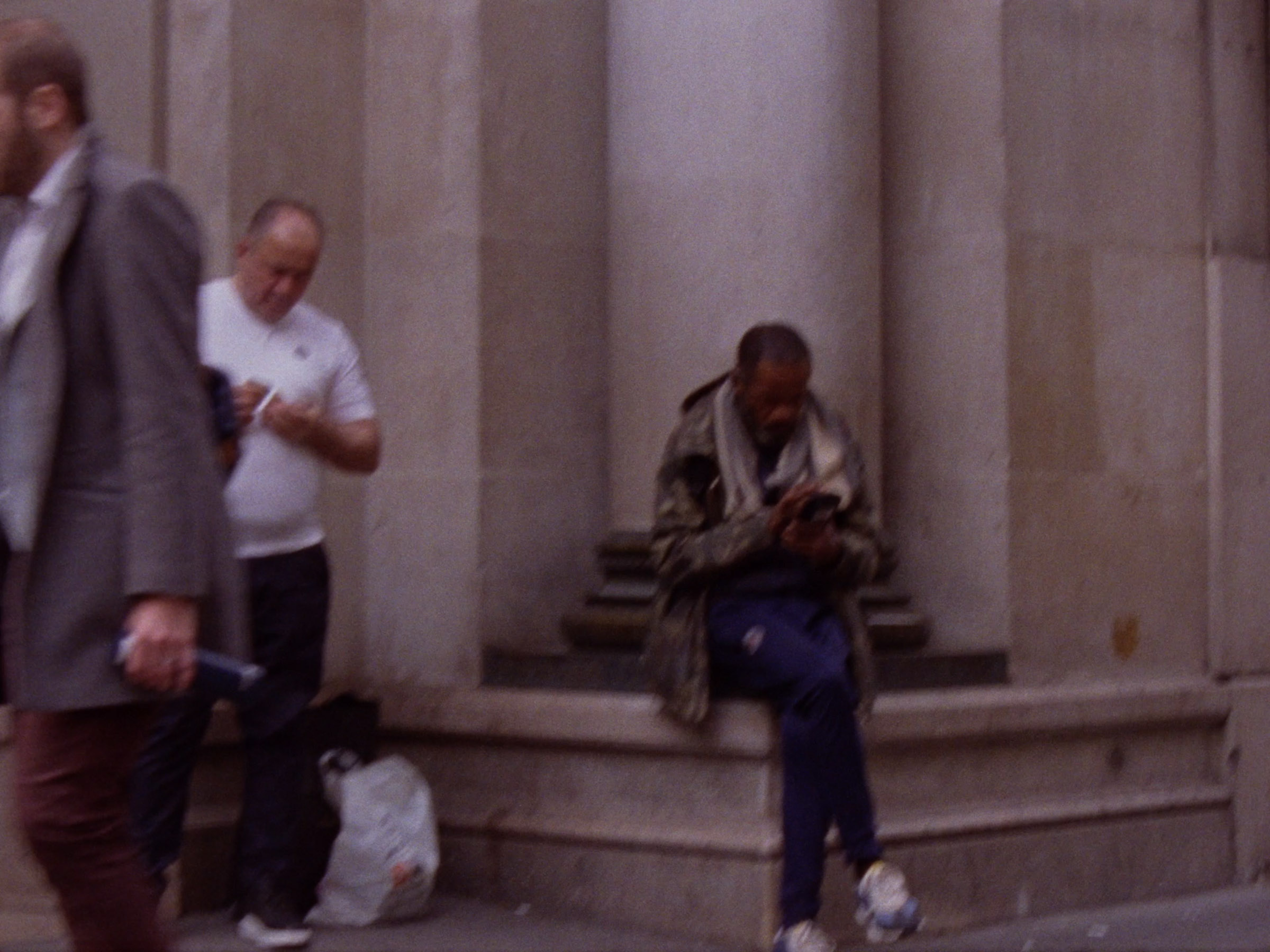 16 mm film still: three men, two of whom checking their phones, in a street of Paris