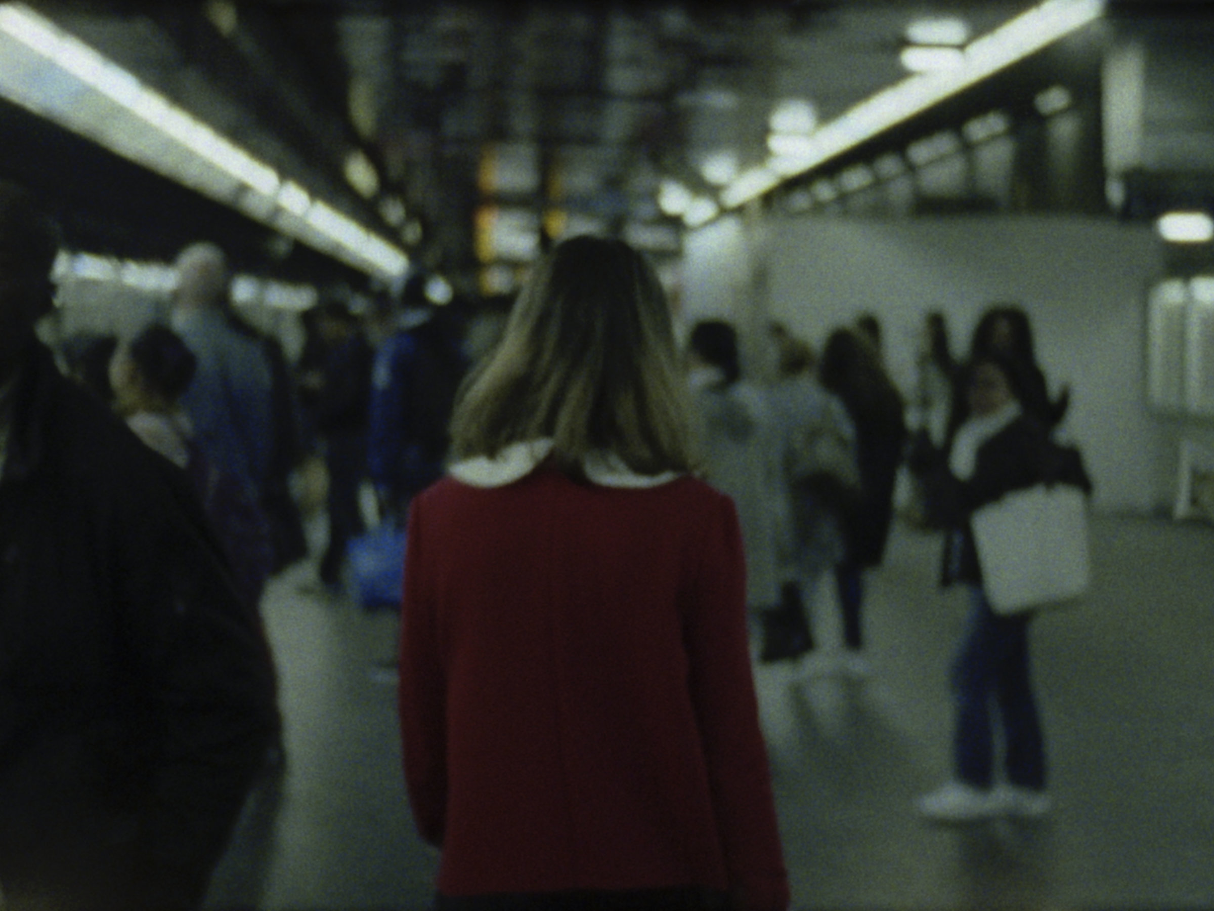 16mm film still: a woman in a red dress walking in a station of the rapid transit system in Paris