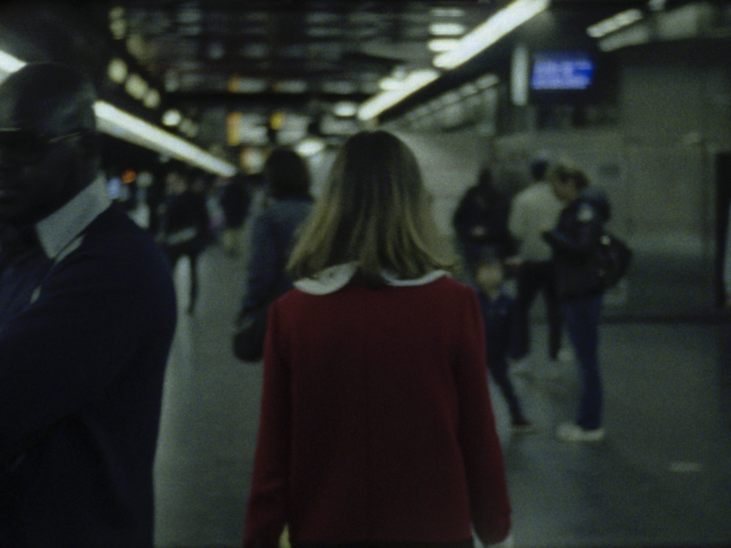 16mm film still: a woman in a red dress walking in a station of the rapid transit system in Paris