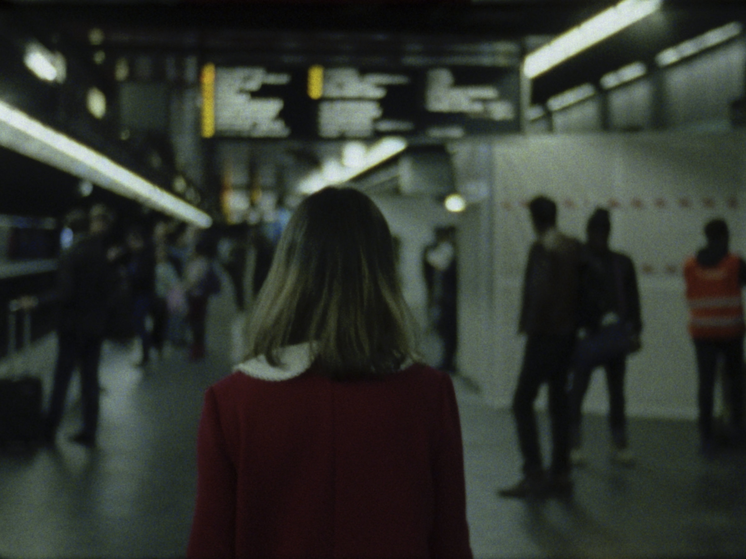 16mm film still: a woman in a red dress walking in a station of the rapid transit system in Paris