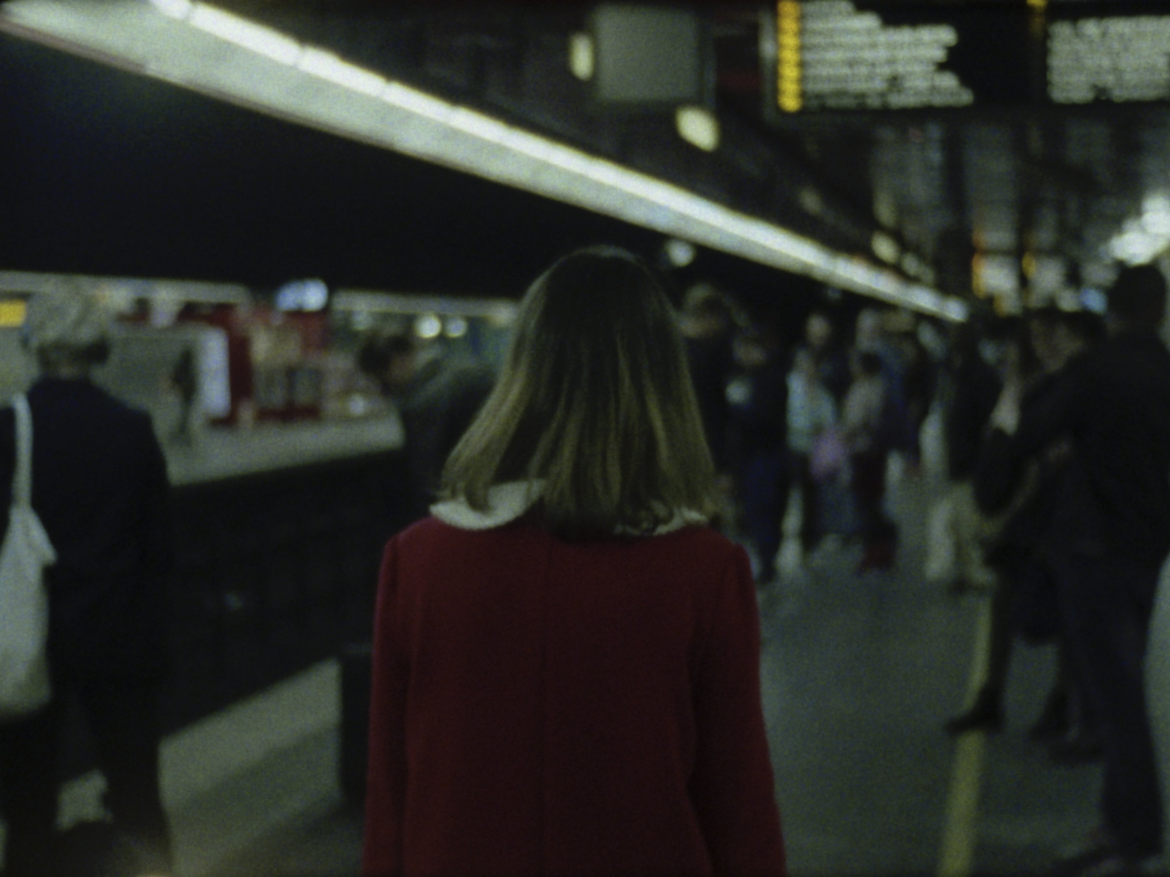 16mm film still: a woman in a red dress walking in a station of the rapid transit system in Paris
