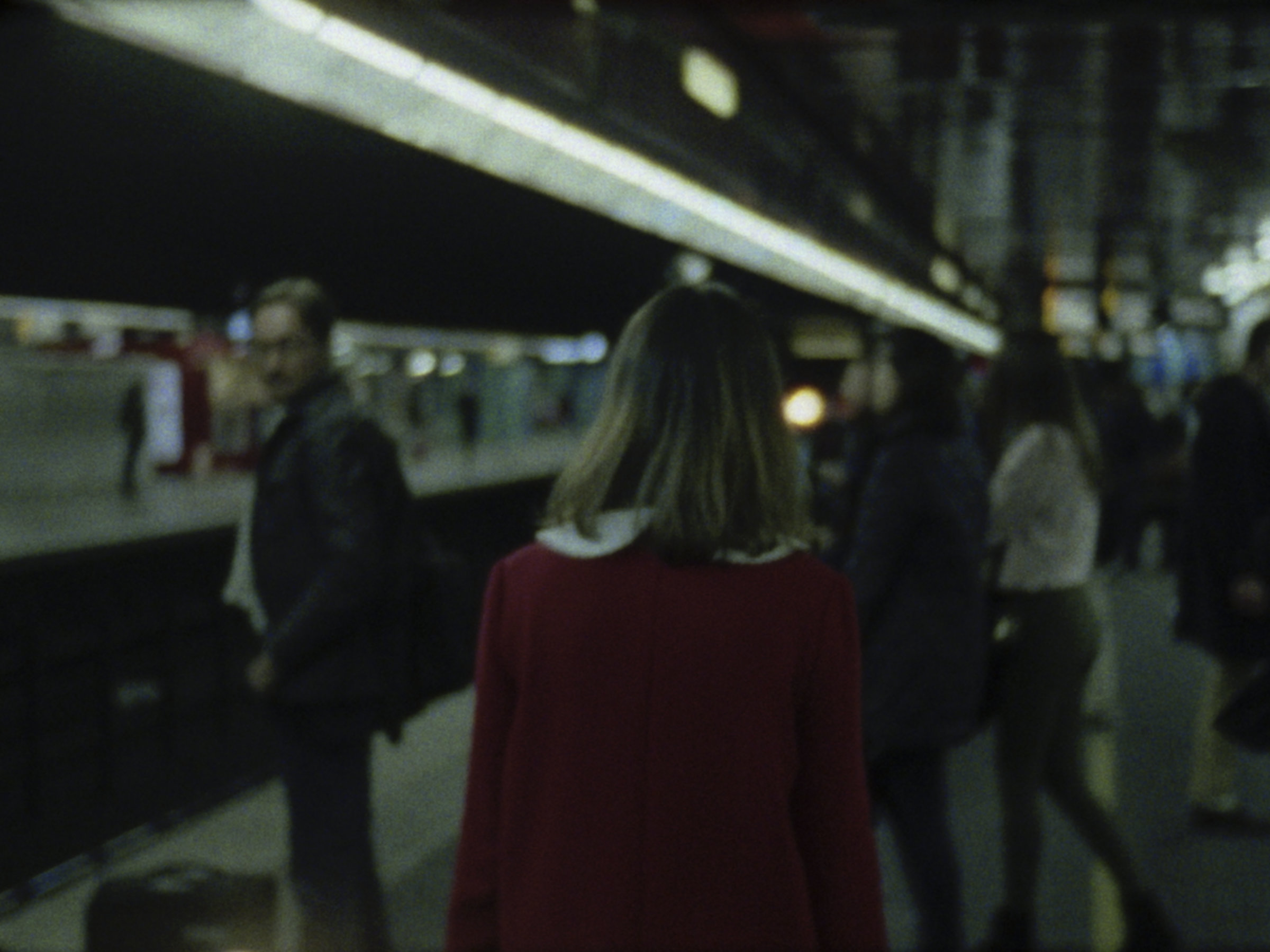 16mm film still: a woman in a red dress walking in a station of the rapid transit system in Paris