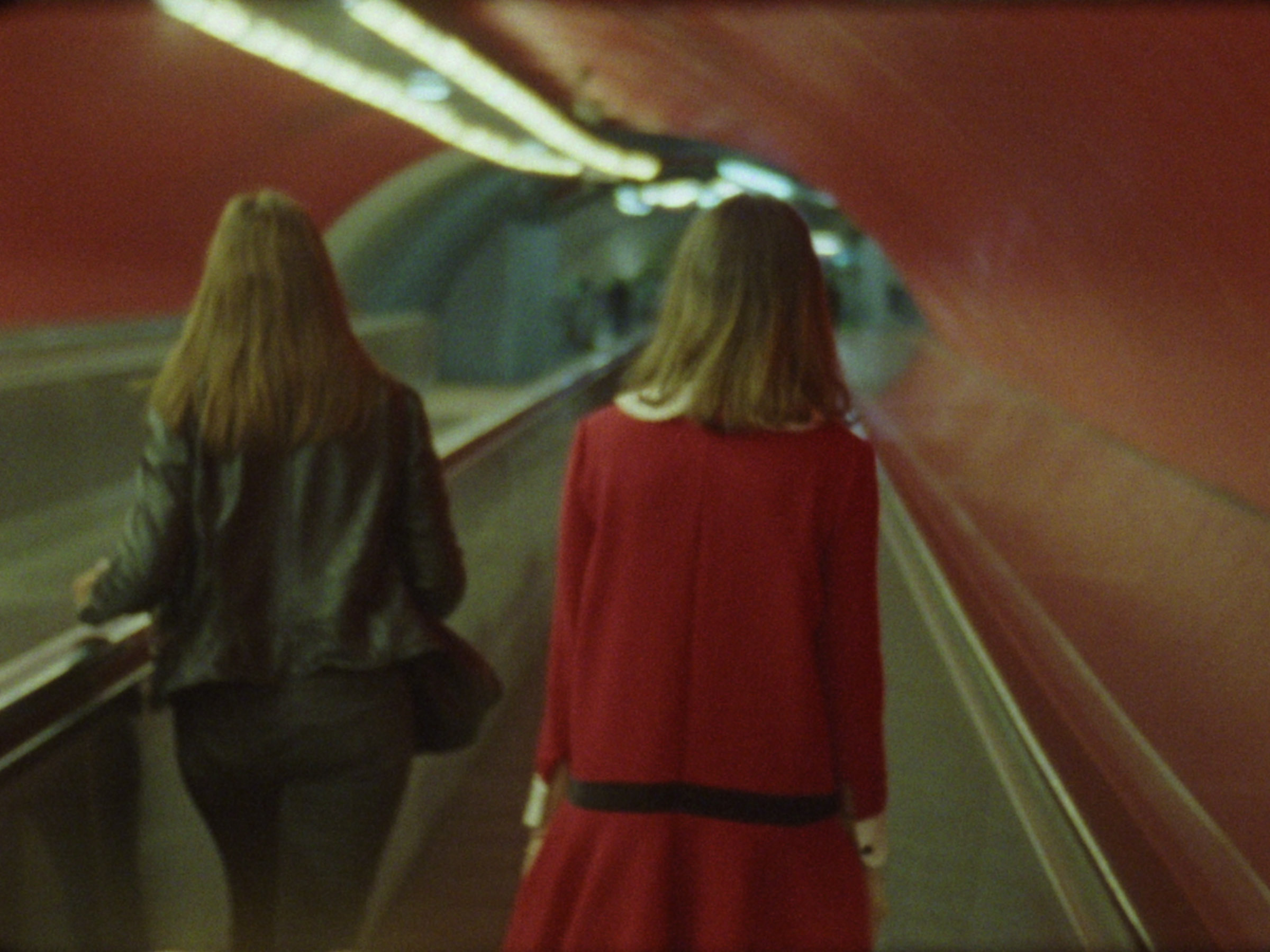 16 mm film still: a woman dressed up as Veruca Salt walking in a red hallway in the Paris metro